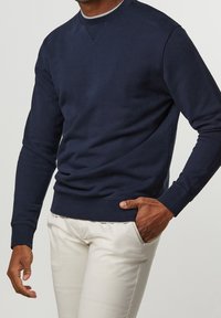 Navyblå sweatshirt med rund halsringning och långa ärmar. Tyget är mjukt med ribbade muddarna och nederkant, och har en diskret triangelsömsdetalj.
