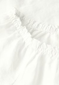 Tessuto bianco con bordo arricciato e volant. Texture morbida, materiale leggero e superficie liscia con una leggera lucentezza.