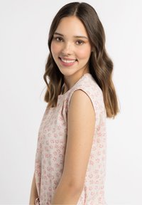 Lichtroze top met bloemmotief, korte mouwen en een ronde halslijn, met kleine bloemenaccenten door de stof heen. Gladde textuur.