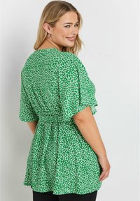 Grön blommig blus med korta ärmar, en cinchad midja och en flödande silhuett. Funktioner små vita blommor över hela tyget.