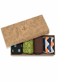 Boîte cadeau avec quatre paires de chaussettes roulées à motifs en noir à pois bleus, motif géométrique vert, marron uni et dessins losanges multicolores.
