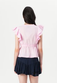 Haut rose à manches courtes avec des manches volantées, taille élastique et ourlet festonné. Associe à une mini-jupe superposée bleu marine foncé.