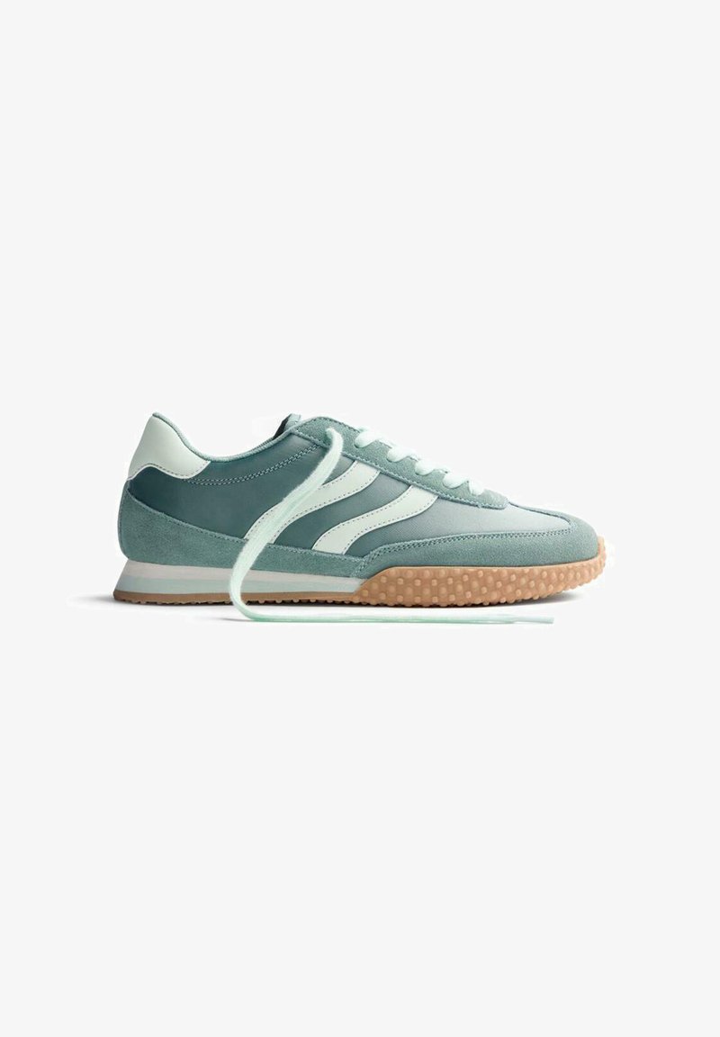 Zapatilla deportiva de color verde azulado claro y blanco con suela de goma, franjas laterales y cordones sueltos, mostrada de perfil sobre fondo blanco.