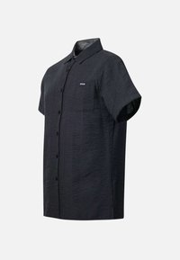 Chemise noire texturée à manches courtes, boutonnée, avec col et poche poitrine étiquetée "Seaside" sur un fond uni.