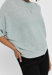 Jasnoszary sweter z prążkowanego dzianego materiału, o szerokim dekolcie i krótkich rękawach, swobodnie opadający na czarne spodnie, z prostym, teksturowanym wzorem.