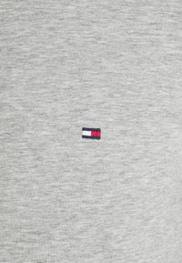 Grijze sweatshirtstof met een zachte textuur, voorzien van een klein geborduurd logo bestaande uit rode, witte en blauwe rechthoeken aan de linkerkant.