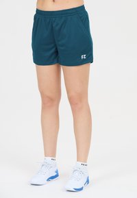 Person iført mørk teal sportshorts med "FZ" logo, hvide sportssko med blå accenter og hvide sokker på en ensfarvet hvid baggrund.