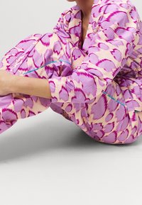 Multifarvet loungewear med et abstrakt mønster i pink og lavendel, med kontrasterende akvamarin-accenter langs sømme og lommer. Blød tekstur.