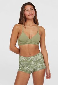 Τοπ μπικίνι ανοιχτού πράσινου χρώματος με σχέδιο τύλιγμα και λεπτές τιράντες, συνδυασμένο με σορτς υψηλής μέσης με λευκό λουλουδάτο μοτίβο.