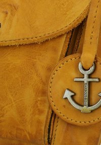 Borsa in pelle gialla con un charm rotondo che presenta un'ancora metallica. La texture notevole mostra una grana morbida e naturale con accenti cuciti.