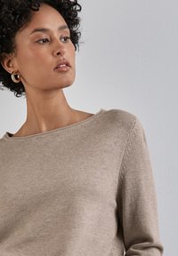 Maglione beige a maglia con una ampia scollatura a barca e maniche lunghe. Presenta una texture liscia e una sottile cucitura lungo le spalle.
