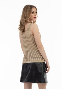 Beige pletený top bez rukávů s openwork designem a výstřihem do V, v kombinaci s černou koženou mini sukní s rozšířenými okraji. Hladké textury a kontrastní barvy.