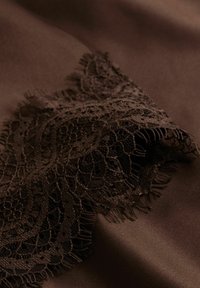 Bruine stof met ingewikkeld zwart kanten randje, met geschulpte randen en delicate bloemmotieven, tegen een gladde, gestructureerde achtergrond.