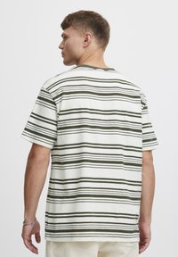 Stripet bomulls t-skjorte i hvit og olivengrønn, rund hals, korte ermer, avslappet passform, med horisontale striper i varierende tykkelse.