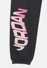 Sorte sweatpants med et pink, tekstureret "JORDAN" logo lodret langs siden, med elastisk talje og manchetter.