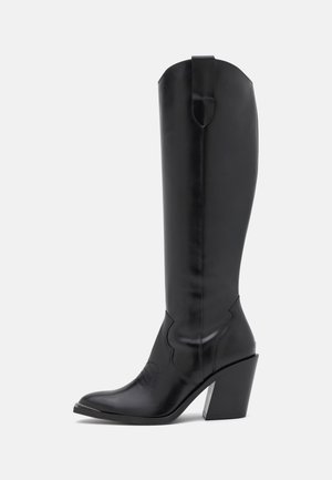 Bota alta hasta la rodilla de cuero negro con punta puntiaguda y tacón bloqueado inclinado, con una lengüeta para tirar en la parte superior y costuras decorativas sutiles.