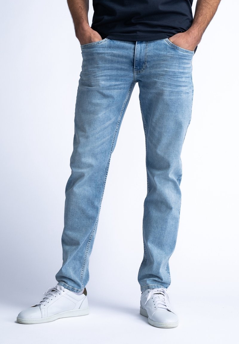 Jeans de mezclilla azul claro con un corte recto en las piernas, que cuentan con bolsillos frontales y detalles descoloridos; combinados con zapatillas blancas.