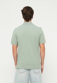 Koszulka polo z krótkim rękawem wykonana z bawełny w jasnym zielonym kolorze. Posiada prążkowany kołnierzyk i szwy, prosty dół oraz boczne rozcięcia. Luźny krój.