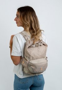 Rucsac bej cu finisaj texturat, curele ajustabile, buzunar frontal cu fermoar și un buton decorativ. Design compact, potrivit pentru utilizare casuală.