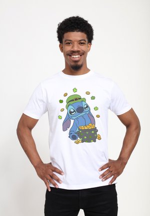 Uomo sorridente che indossa una maglietta bianca con un fumetto di Stitch con cappello da leprechauno che tiene una pentola di monete d'oro ed è circondato da trifogli e monete.