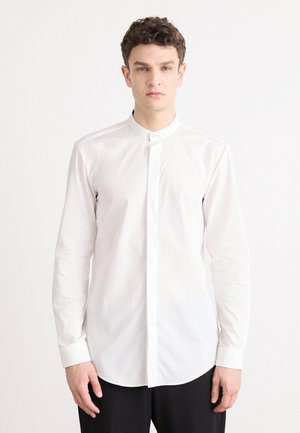 Camisa blanca de botonadura con un collar alzado; tejido de algodón suave; mangas largas; ligero brillo; dobladillo redondeado; diseño minimalista.