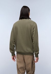 Olivengrøn sweatshirt med rund halsudskæring, ribstrikkede manchetter og kant; bæres med lysebrune cargo-bukser. Stoffet ser blødt og tekstureret ud.