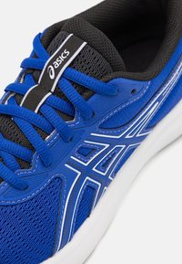 Chaussure de sport bleue avec une tige en maille et des accents noirs. Présente des coutures blanches et un logo sur la languette, avec des lacets plats pour un ajustement sûr.