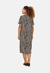 Kurzärmliges, knielanges Kleid im beige-schwarzen Zebra-Muster, mit lässiger Passform und weichem Stoff, getragen mit dunkelbraunen Slippern.