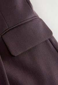 Dunkellila Stoff mit gerippter Textur, versehen mit einer Klapptasche auf der Vorderseite, sauberen Nähten und glatten Konturen.