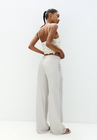 Lys grå vide ben bukser lavet af blødt stof, med baglommer og en mellemhøj talje, parret med en hvid lace crop top med justerbare stropper.