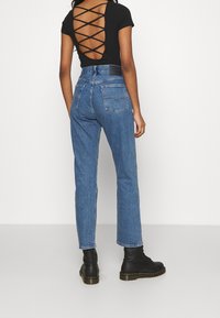 Top negro de manga corta con diseño de espaldas entrelazadas, combinado con jeans de mezclilla azul de tiro alto y botas de tobillo negras con cordones.