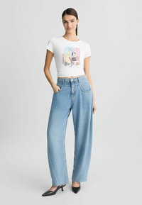 T-shirt blanc court avec un graphique coloré de la silhouette de New York, associé à un jean large bleu et des talons noirs à bout pointu.