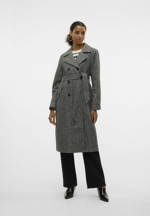 Manteau trench gris en laine avec un devant double boutonnière, une taille ceinturée, un col cranté et des poches latérales, associé à un pantalon large noir et des chaussures.