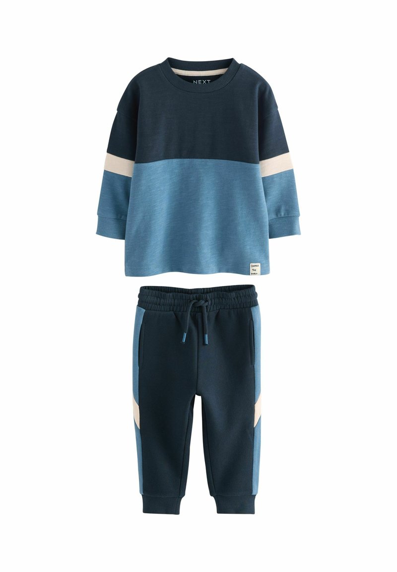 Zweiteiliges Kinderoutfit in Blautönen. Langärmliges Oberteil mit horizontalen Farbschlägen; die Hose hat einen Kordelzug und seitliche Akzente.