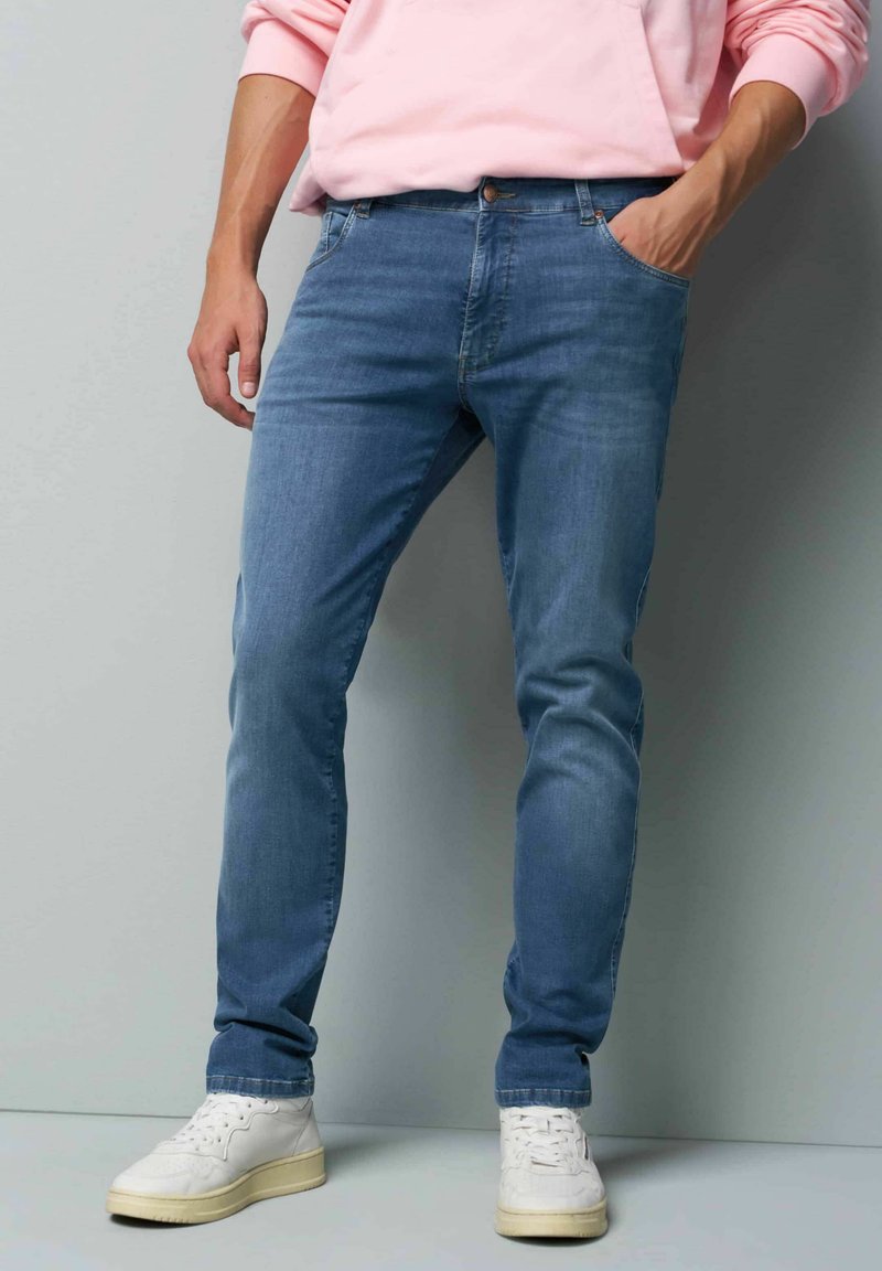 Lichtblauwe denim jeans, slim fit, met een vijfzakkenontwerp. Gepaard met witte sneakers. De stof lijkt iets versleten.
