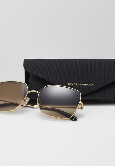 Goldfarbene Sonnenbrille mit braunem Verlaufsglas, präsentiert neben einem schwarzen, strukturierten Etui mit der Aufschrift "DOLCE & GABBANA." Sechseckige Form.