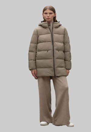 Chaqueta de plumón beige con un diseño acolchado, cierre con cremallera y capucha. Combinada con pantalones de pierna ancha marrón claro y zapatos blancos.