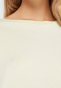 Prenda de algodón suave de color amarillo claro, con un amplio escote barco y una textura lisa, mostrando detalles de costura mínimos en el dobladillo.