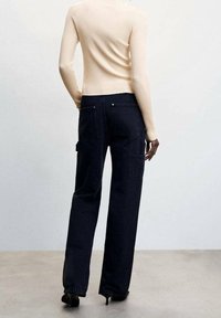 Schwarze Cargo-Hosen mit großen Seitentaschen, im geraden Schnitt und Denim-Textur. Kombiniert mit einem hellen, gerippten Langarmoberteil.