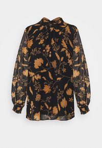 Blouse noire transparente avec un motif floral doré, dotée d'un col haut, de longues manches bouffantes et de poignets froncés.