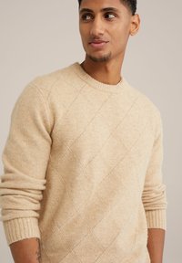 Beige gestrickter Pullover mit einem strukturierten Diamantmuster, Rundhalsausschnitt und gerippten Bündchen. Aus einem weichen, warmen Material hergestellt.