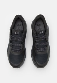 Chaussures de sport noires avec une tige en maille texturée, des lacets ton sur ton et une semelle à motifs. Présente des accents de logo sur la languette et sur le côté.