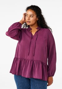 Blusa lunga a maniche con scollo a V, collare arricciato e orlo smerlato. Realizzata in tessuto leggero, presenta una vestibilità ampia.