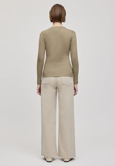 Langarmige, getailleerde, beige top met ronde hals, gecombineerd met wijde, lichtbeige broek en eenvoudige, stijlvolle schoenen.