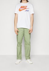 Vit bomullst-shirt med flerfärgat "NIKE"-logotyp. Ljusgröna cargobyxor med fickor. Vita sneakers. Enkel och avslappnad design.