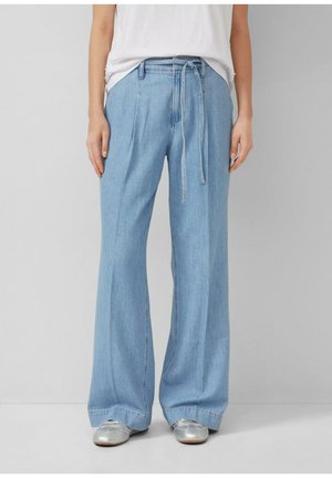 Hellblaue Jeans mit weitem Bein und einem Stoffgürtel, der in der Taille gebunden ist, kombiniert mit silbernen Schuhen und einem weißen, eingesteckten Oberteil.