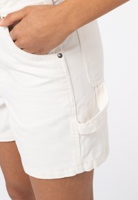 Shorts in denim bianco con una finitura testurizzata, dotati di tasche laterali e dettagli in metallo a scatto, che mostrano un design aderente e linee pulite.