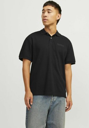 Polo shirt noir à manches courtes, dotée d'un col et d'un motif imprimé subtil sur la poitrine. Associée à un jean bleu clair.