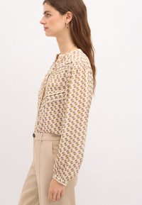 Blusa leggera in crema con motivo floreale nei toni del rosa e del verde, maniche lunghe con polsini elasticizzati e chiusura con bottoni.