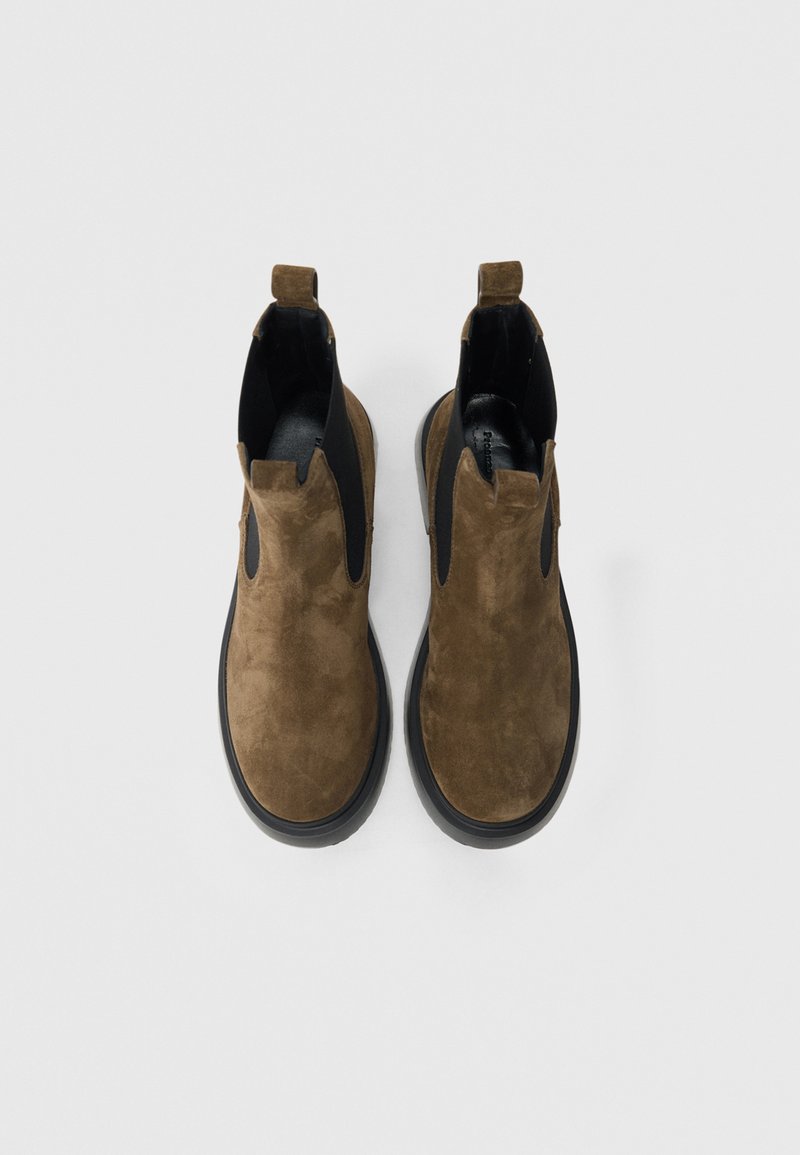 Stivaletti Chelsea in camoscio marrone con pannello elastico nero, punta arrotondata e suola in gomma nera. Dotati di due linguette per facilitare la calzata.